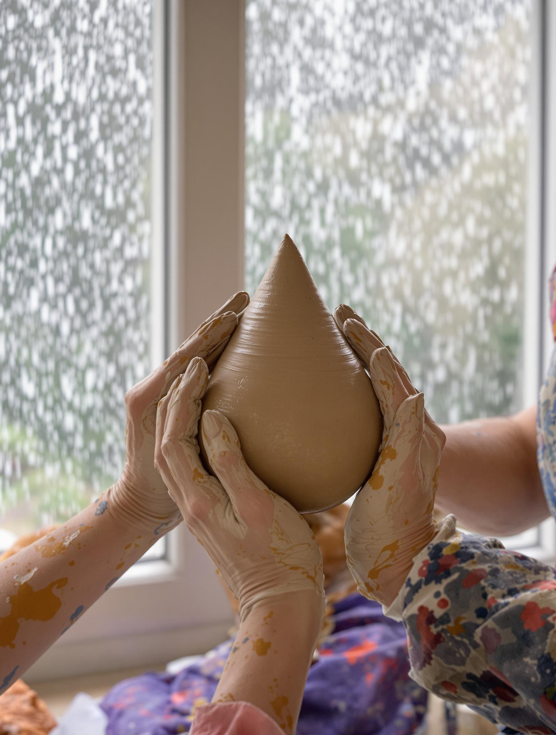 Atelier poterie adulte avec des mains modelant une goutte d’argile.